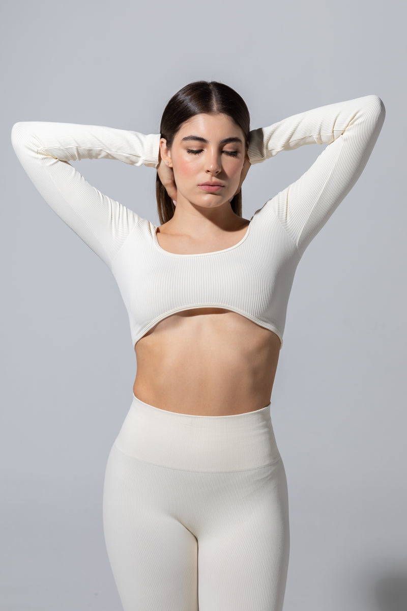 Model wearing The Seamless Long Sleeve Top in cream with cream leggings, hands behind head