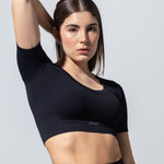 Model in The Seamless Crop Top in black, one arm raised, three-quarter view
