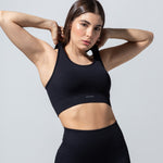 Model in The Seamless Bra Top in black, hands behind head, three-quarter view