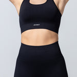 Close-up of The Seamless Bra Top in black, arms raised, showing the ribbed underband